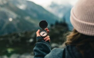 Femme de dos qui tient une boussole pour s'orienter dans la nature.