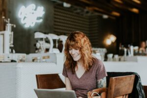 Femme rousse assise dans un café et qui travaille avec le sourire.